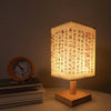 A Chinese style dimmable table lamp with a woven linen shade sits on a wooden base next to a stack of books.