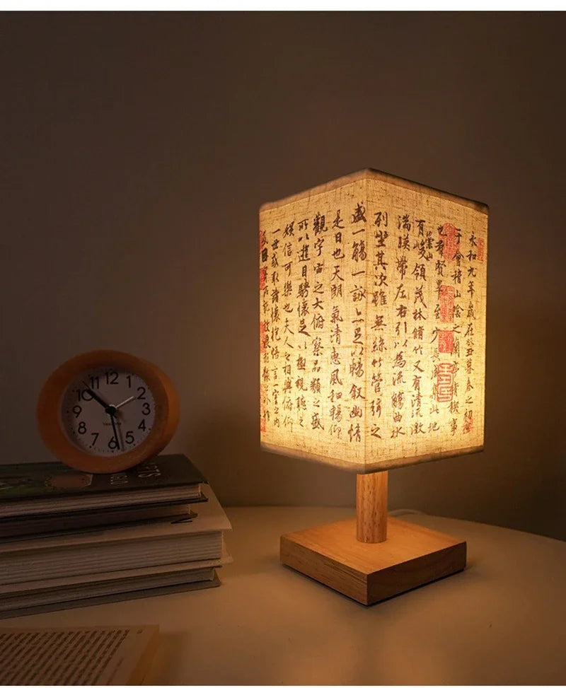 A Chinese style dimmable table lamp with a woven linen shade sits on a wooden base next to a stack of books.