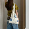 A person is holding a white handwoven knit tote bag with blue geometric patterns in a natural light setting.