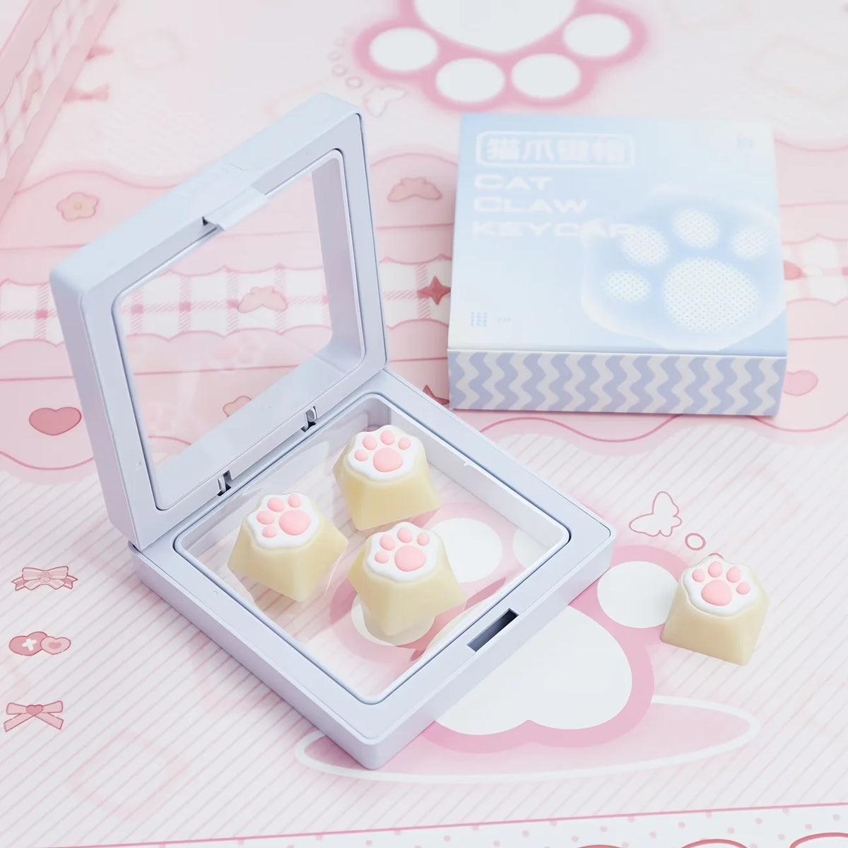A white silicone keycap set featuring cat paw shapes and pink hearts displayed in an open case.