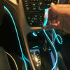 A hand is holding a flexible blue LED light strip inside a car interior, illuminating the dashboard and console.