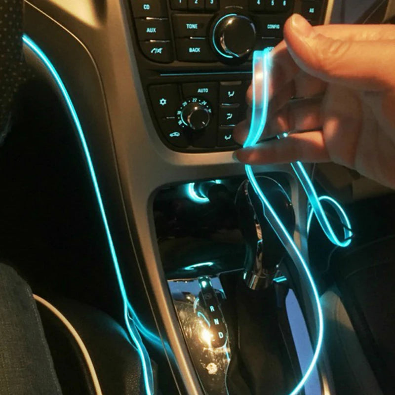 A hand is holding a flexible blue LED light strip inside a car interior, illuminating the dashboard and console.