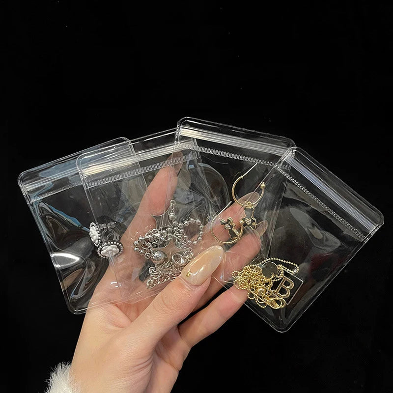 A hand holds a clear plastic jewelry pouch with a zip lock closure, containing silver and gold-toned necklaces.