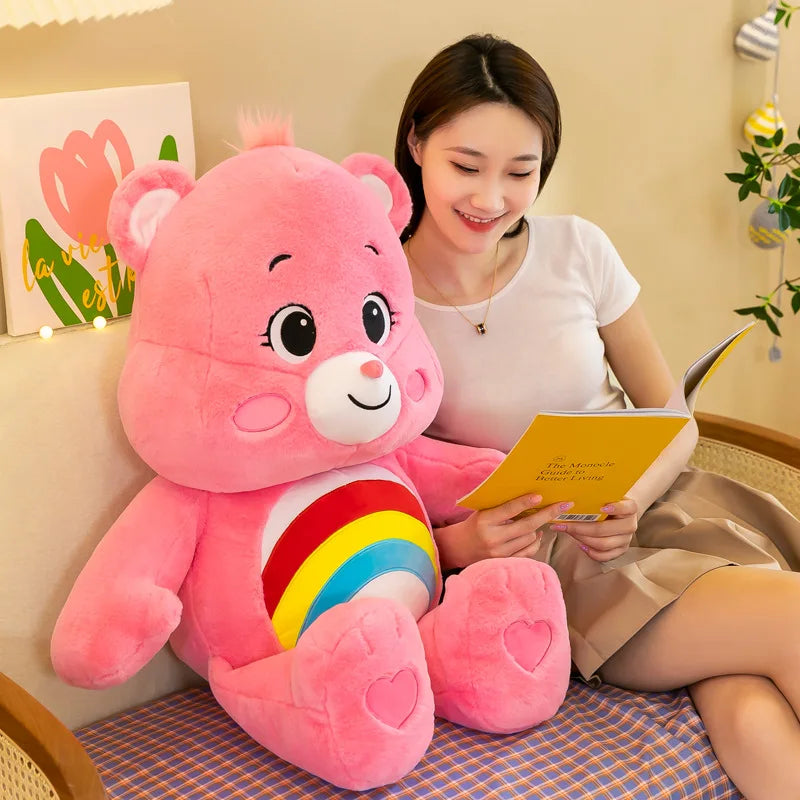 Una mujer sostiene un peluche Kawaii Rainbow Care Bears rosa mientras está sentada en una alfombra estampada.