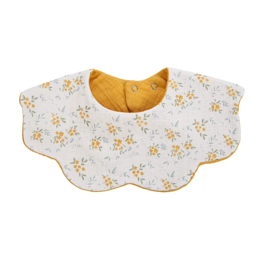 A white muslin cotton baby bib with a yellow lining and adjustable snap closure.
