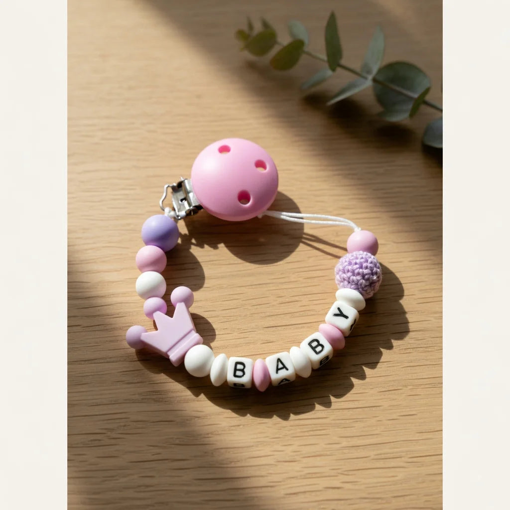 A pink silicone baby pacifier clip with a purple accent is displayed on a wooden surface.