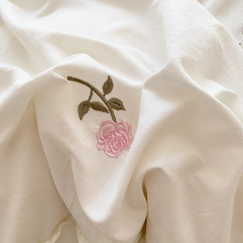 Close-up of a cream fabric featuring a delicate embroidered rose in pink and green thread.
