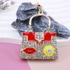 A crystal rhinestone handbag keychain with a red and gold design is displayed against a gray textured background.