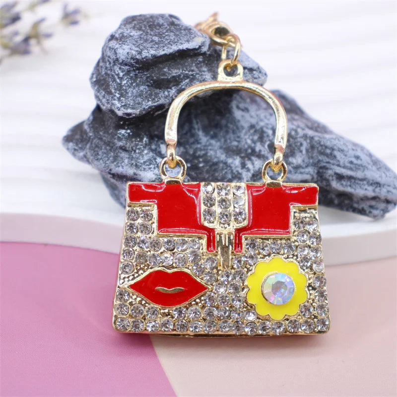 A crystal rhinestone handbag keychain with a red and gold design is displayed against a gray textured background.