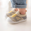 A pair of beige and yellow breathable soft-sole baby shoes with non-slip grip worn on a person's foot.