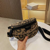 Eine Hand hält eine schwarz-goldene Leopardenmuster-Crossbodytasche auf einer weißen Oberfläche.