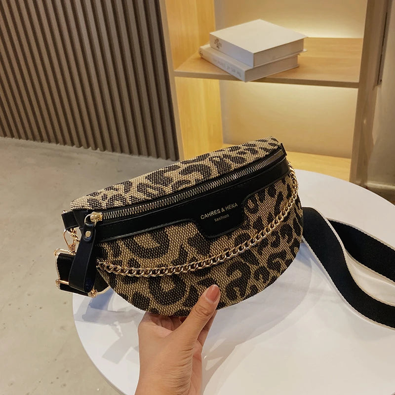Eine Hand hält eine schwarz-goldene Leopardenmuster-Crossbodytasche auf einer weißen Oberfläche.