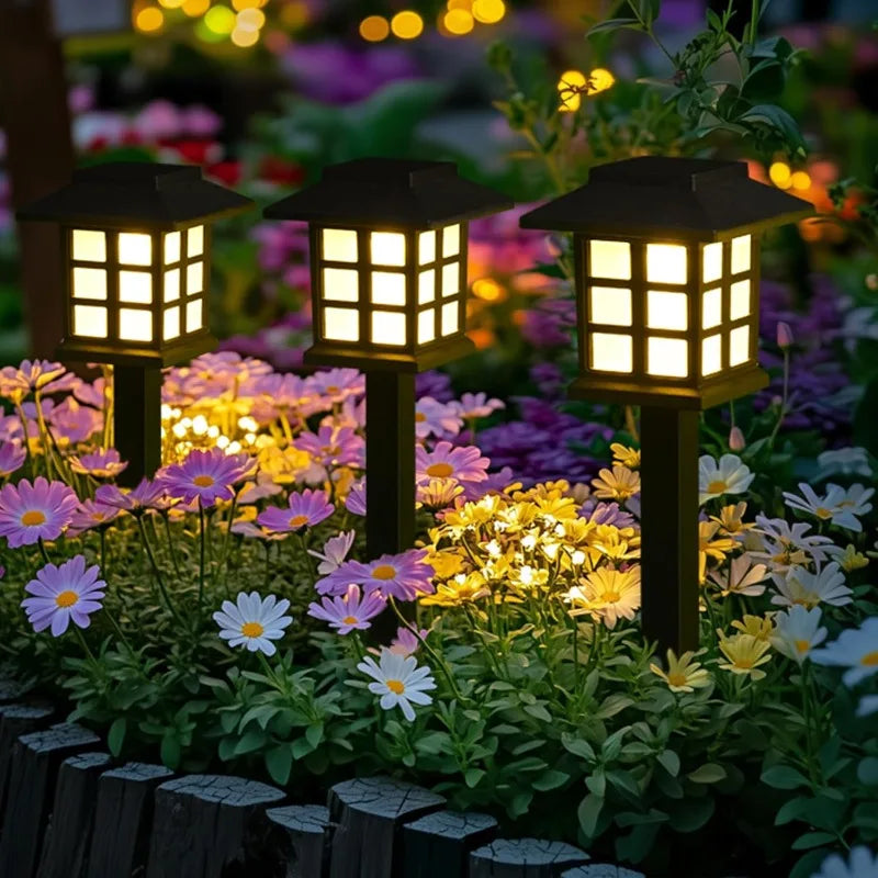 Deux lampes solaires noires illuminent un massif de fleurs violettes et jaunes la nuit.