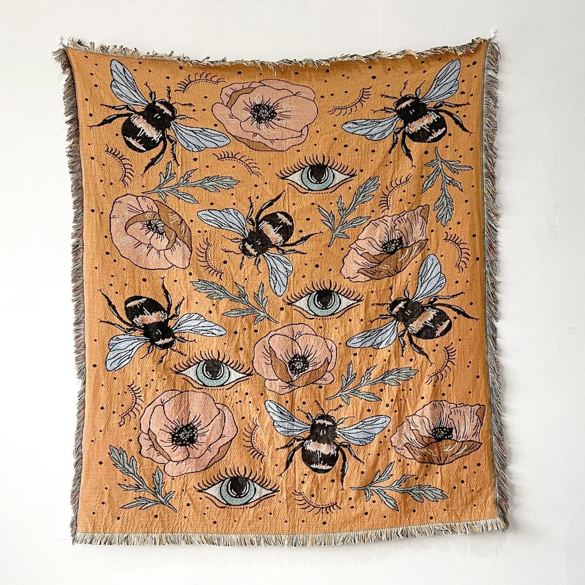 A woven throw blanket featuring a bohemian pattern of bees and floral elements in earthy tones.
