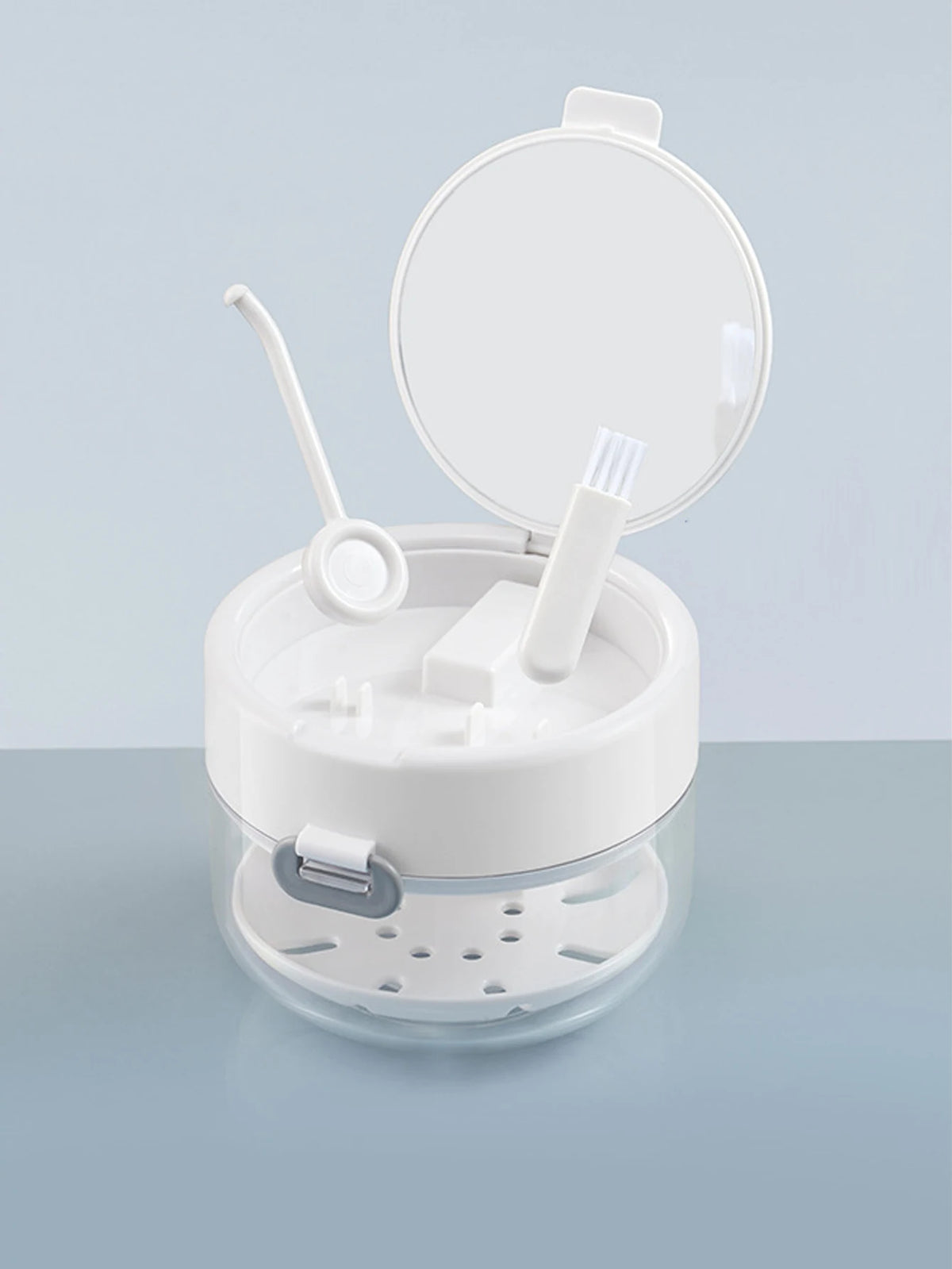 A clear portable denture case with a lid open, showing a cleaning brush and storage components.