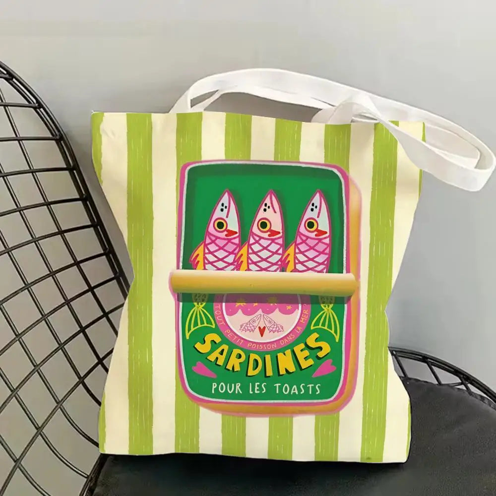 A canvas tote bag featuring a vibrant illustration of three sardines on a green background with vertical stripes.