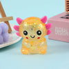 A small, squishy, translucent yellow axolotl stress ball with pink horns resting on a light blue surface.