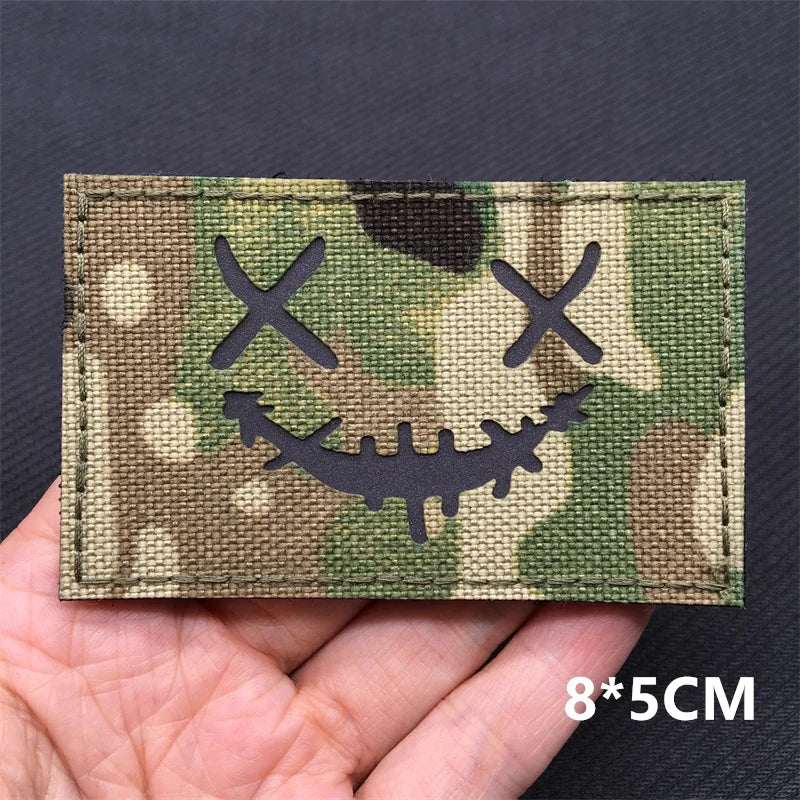A rectangular camouflage tactical patch featuring a skull and crossbones design on a green and brown background.