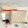 A cream-colored quilted makeup bag with a red heart pattern is shown next to a white tube and a small black item.