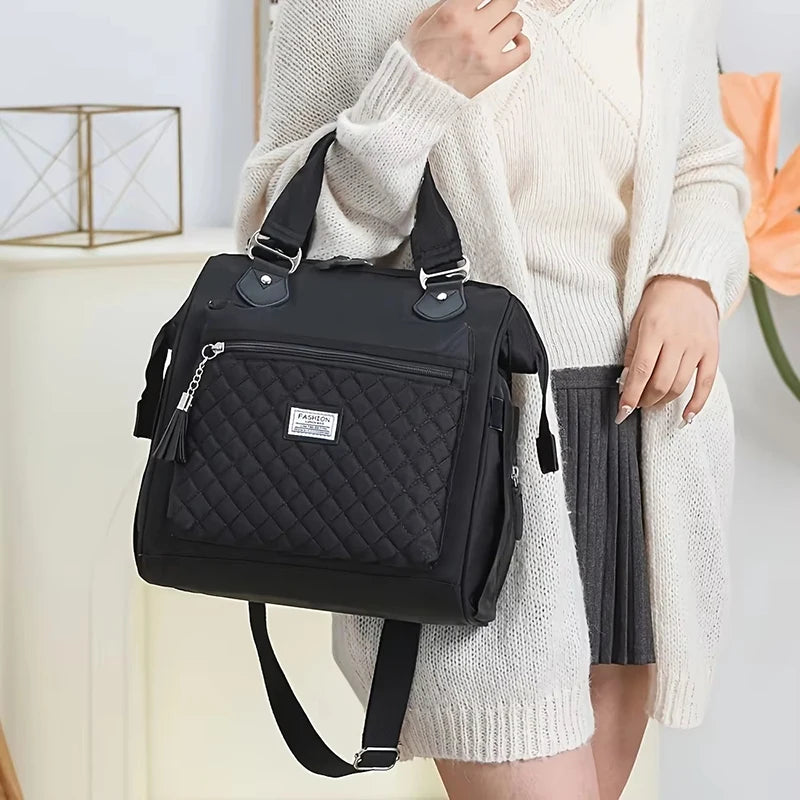 Eine Frau hält eine schwarze isolierte Thermotasche mit gestepptem Muster und Riemen vor hellem Hintergrund.