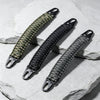 A close-up of a thick, braided paracord handle with metal hooks resting on a light gray stone surface.