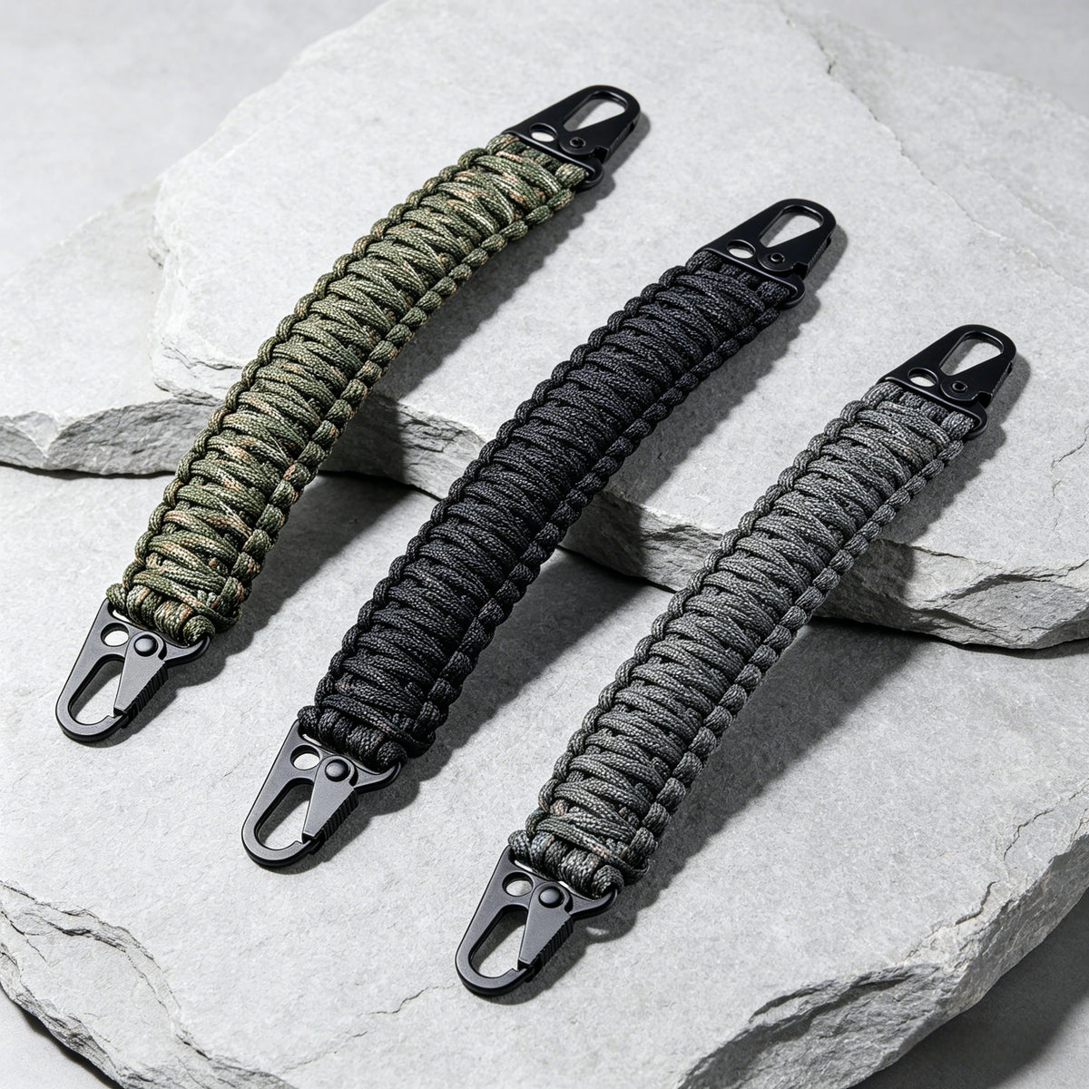 A close-up of a thick, braided paracord handle with metal hooks resting on a light gray stone surface.