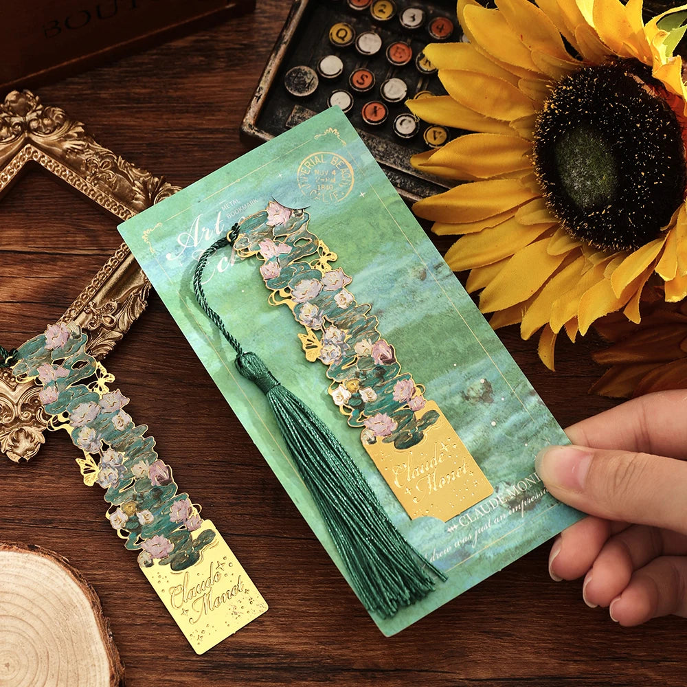 A vintage metal bookmark with an artistic hollow design and green tassel resting on a wooden surface next to a sunflower.