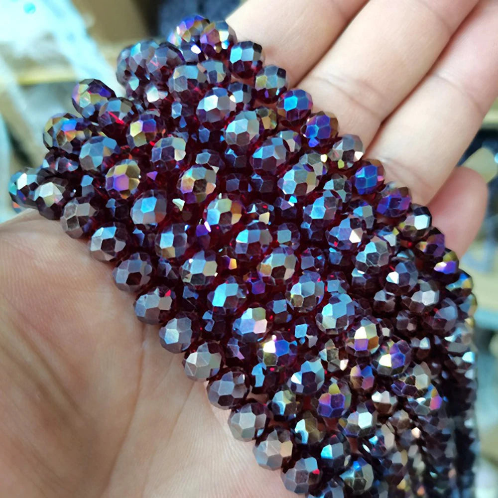 A hand holds a string of faceted crystal glass spacer beads with deep purple and ruby tones.