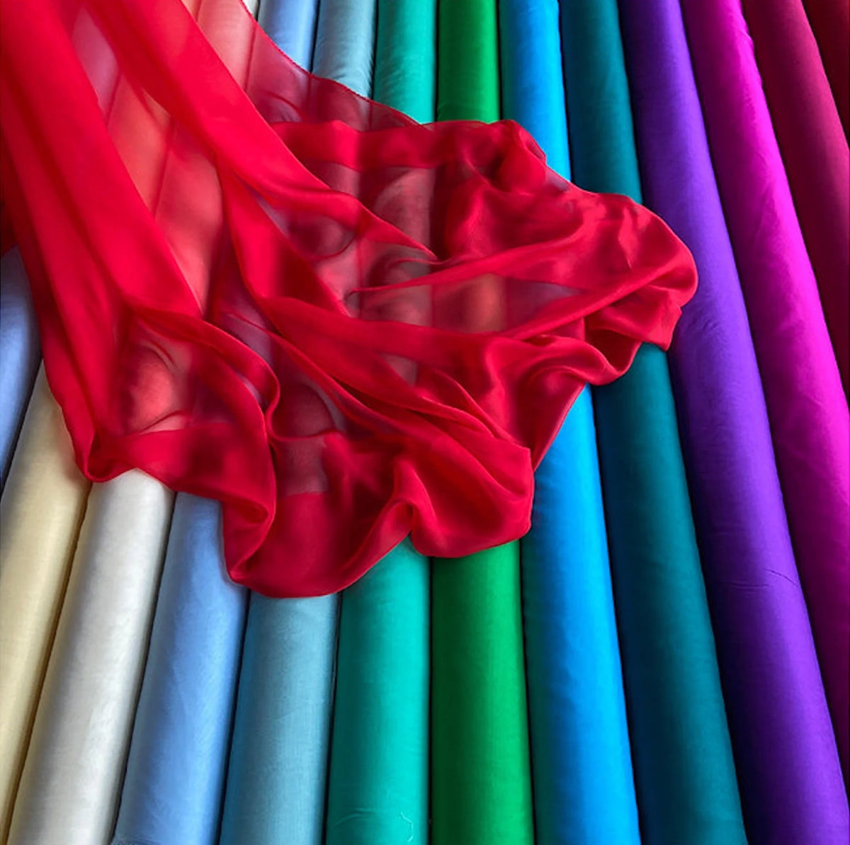 A vibrant collection of sheer red and purple silk chiffon fabric rolls displayed vertically.