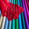 A vibrant collection of sheer red and purple silk chiffon fabric rolls displayed vertically.