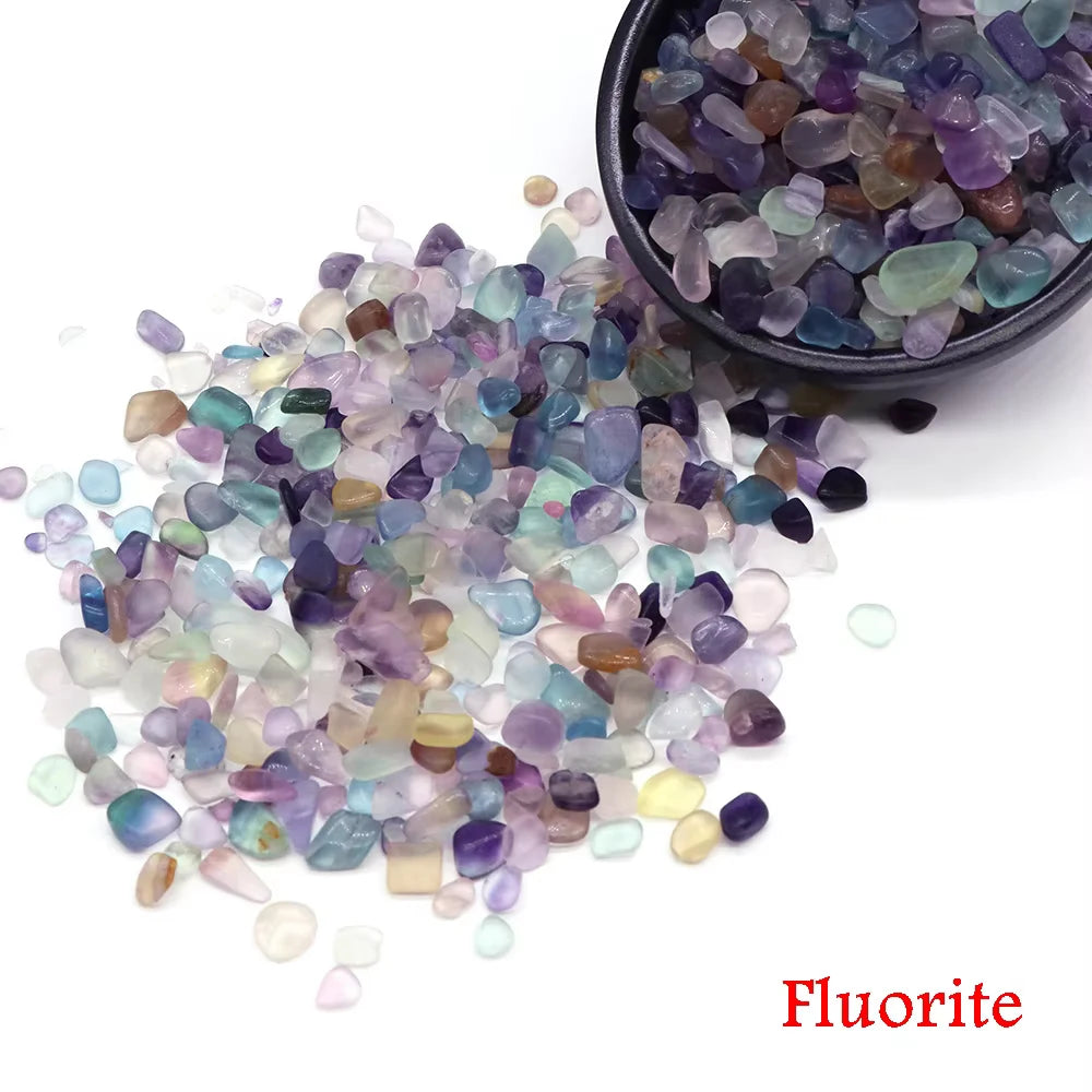 A pile of various colored fluorite crystal chips and tumbled stones in a dark bowl.