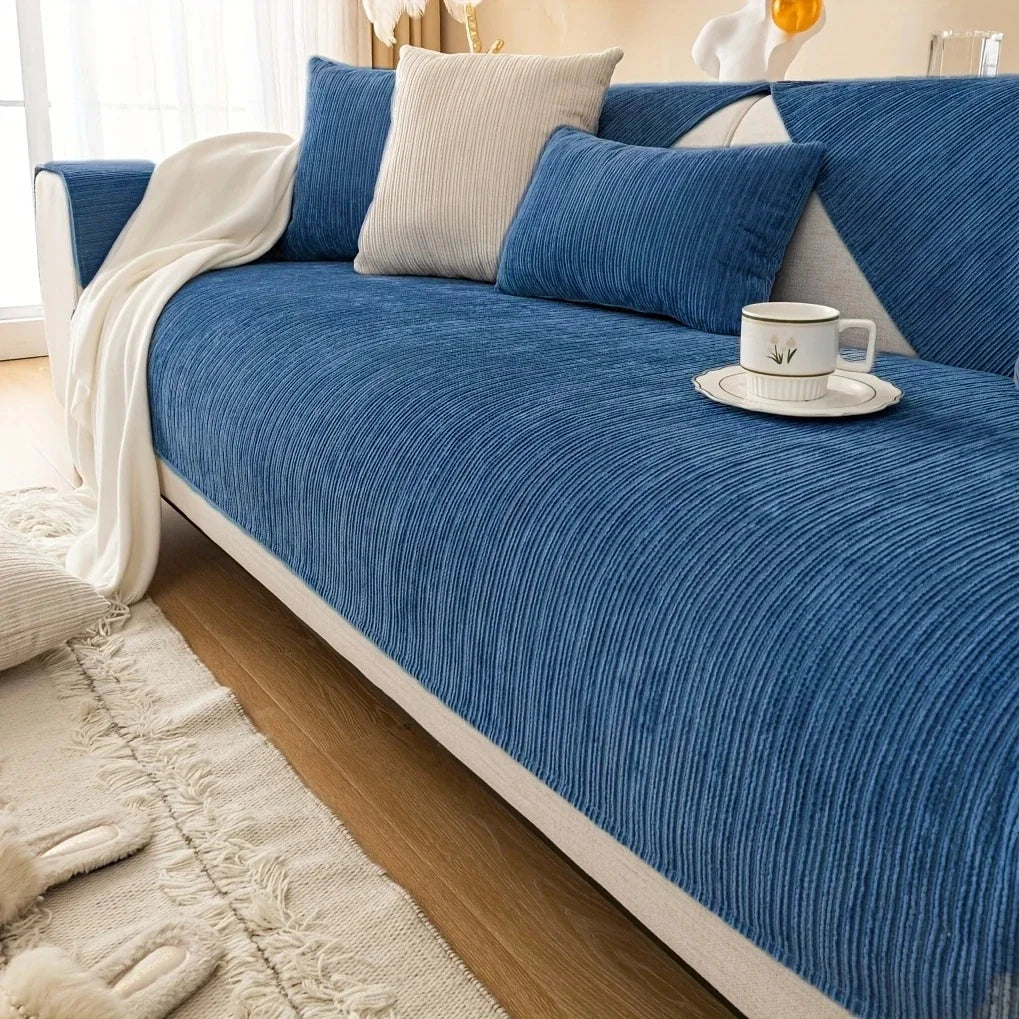 A deep blue geometric sofa cushion cover with light gray accent pillows and a white throw blanket on a wooden floor.