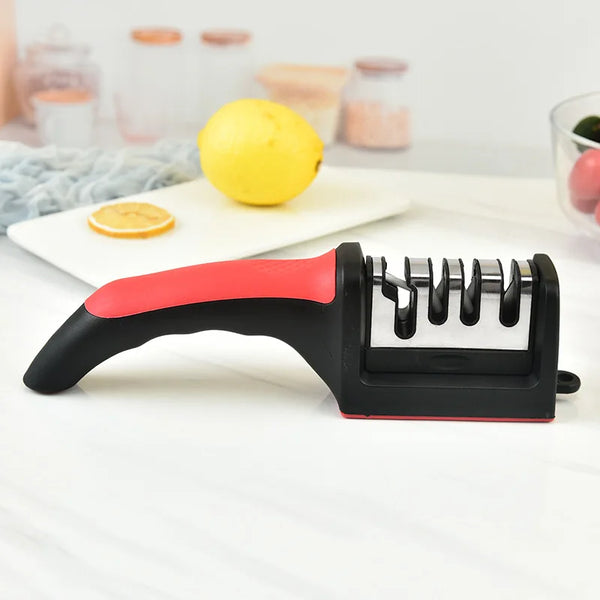 A black and red handheld knife sharpener is shown next to a lemon and orange on a white surface.