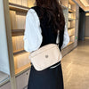 A woman wearing a black dress and white shirt carries a beige nylon crossbody bag in a modern hallway.