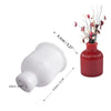 White silicone mold with a base and a round top, shown next to a red vase with dried flowers.
