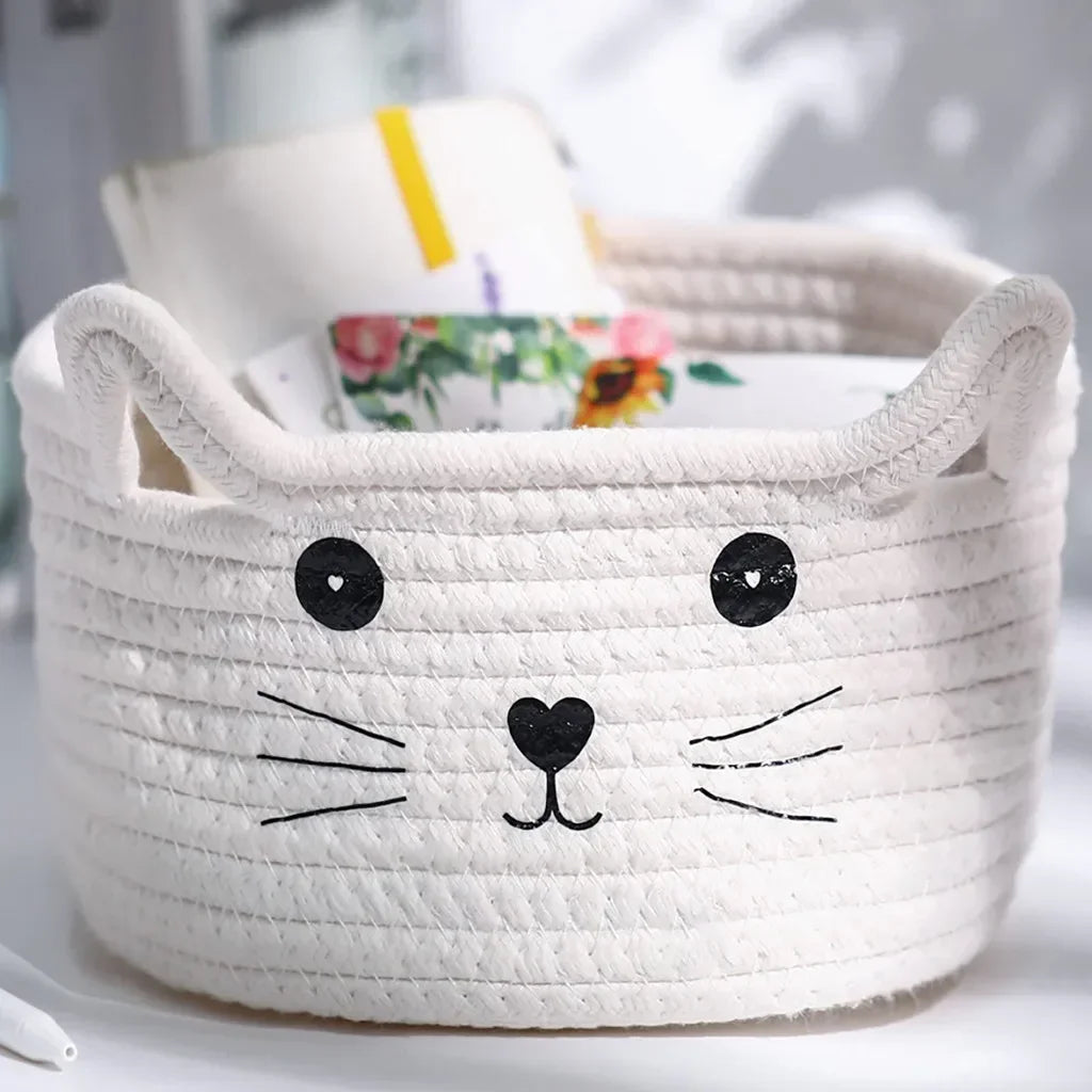 A white woven cotton rope storage basket shaped like a cat's face with black features.
