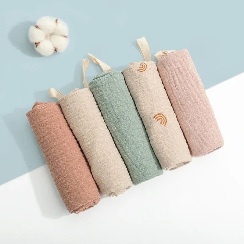 A collection of soft cotton gauze burp cloths in various pastel shades, including pink, beige, and mint green.