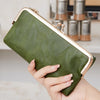 A hand holds a olive green leather wallet with gold accents against a blurred background.