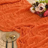 Orange ruffled cotton gauze table runner draped in soft folds with floral greenery