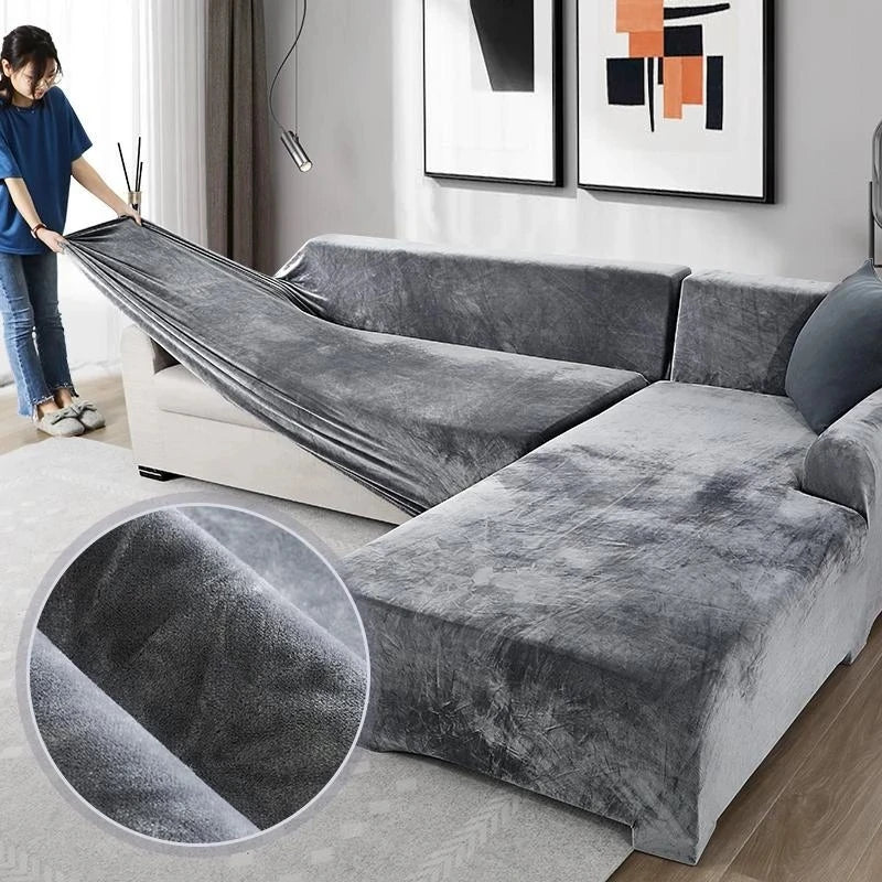A person is draping a plush gray velvet elastic sofa cover over an L-shaped sofa.