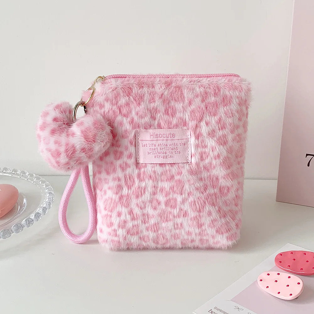 A pink faux fur cosmetic bag with a leopard print texture and a pink pom-pom charm.