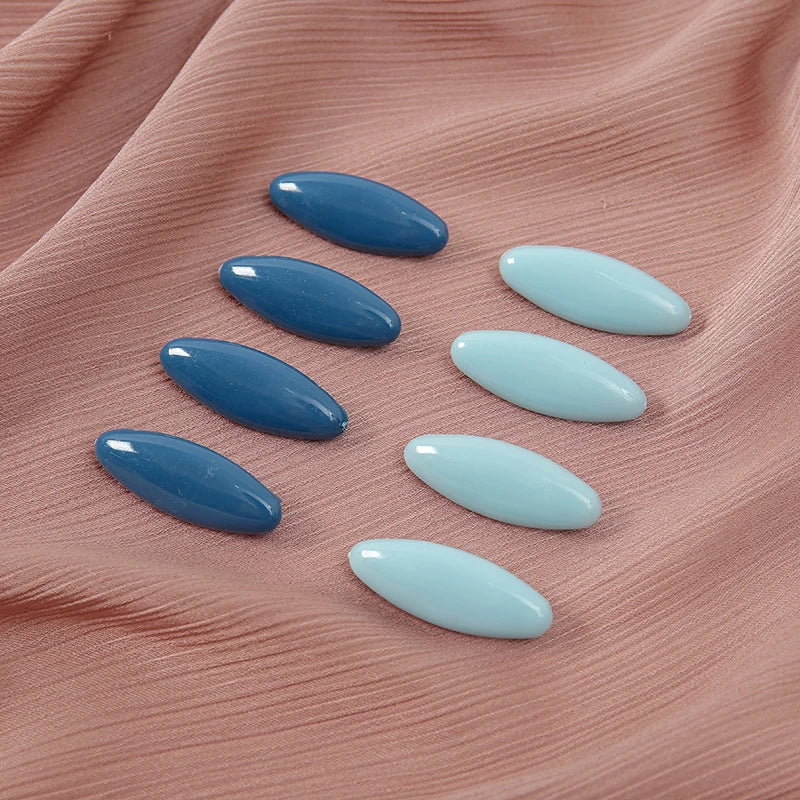 A set of eight oval solid color scarf pins in shades of blue and light blue arranged on a pink fabric.