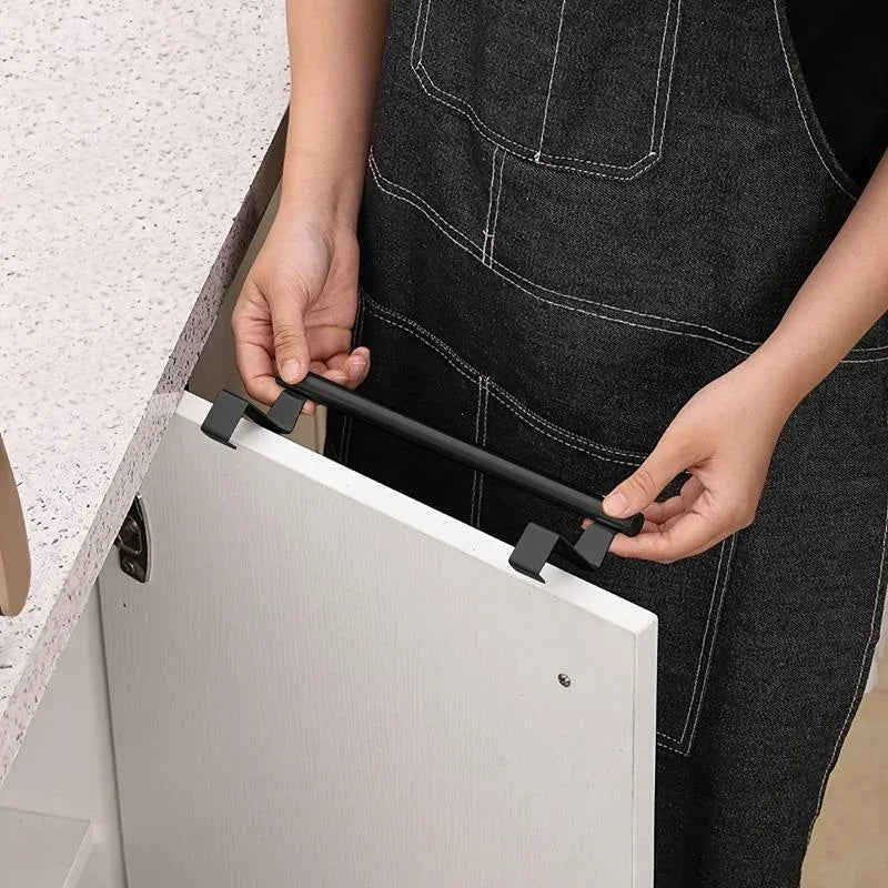 A person is installing a black punch-free over-cabinet towel rack onto a white cabinet door.