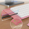 A pink acrylic keyboard stand with a non-slip silicone strip and memory foam wrist rest shown on a wooden desk.