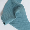 A close-up of a teal organic cotton muslin baby bib with an absorbent bandana folded and draped.