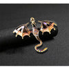 A detailed enamel dragon brooch featuring iridescent scales and rhinestone accents on a black background.