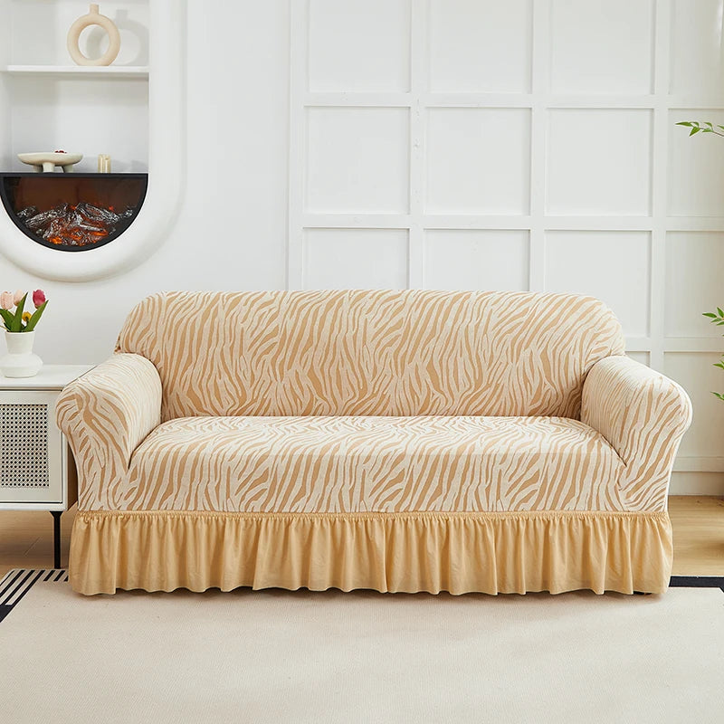 A beige jacquard sofa cover with a striped pattern and an elastic skirt displayed in a bright room.