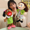 A soft plush full-body hand puppet resembling a child with brown skin and dark hair, dressed in green clothing.