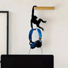 A black monkey silhouette is hanging from a wooden wall hook above a pair of blue headphones.