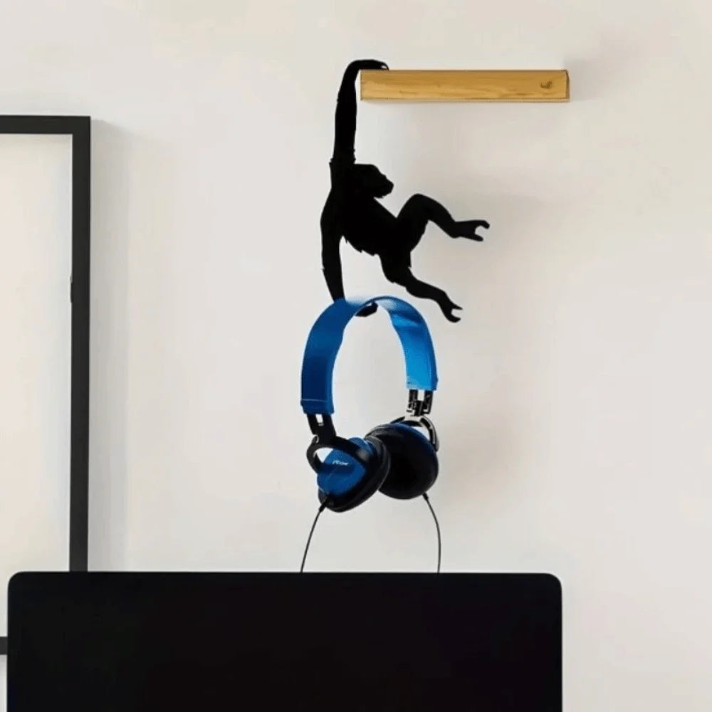 A black monkey silhouette is hanging from a wooden wall hook above a pair of blue headphones.